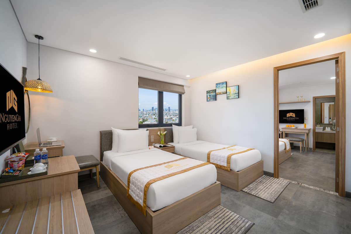 A hotel room with two beds, a desk, a TV, and a city view.