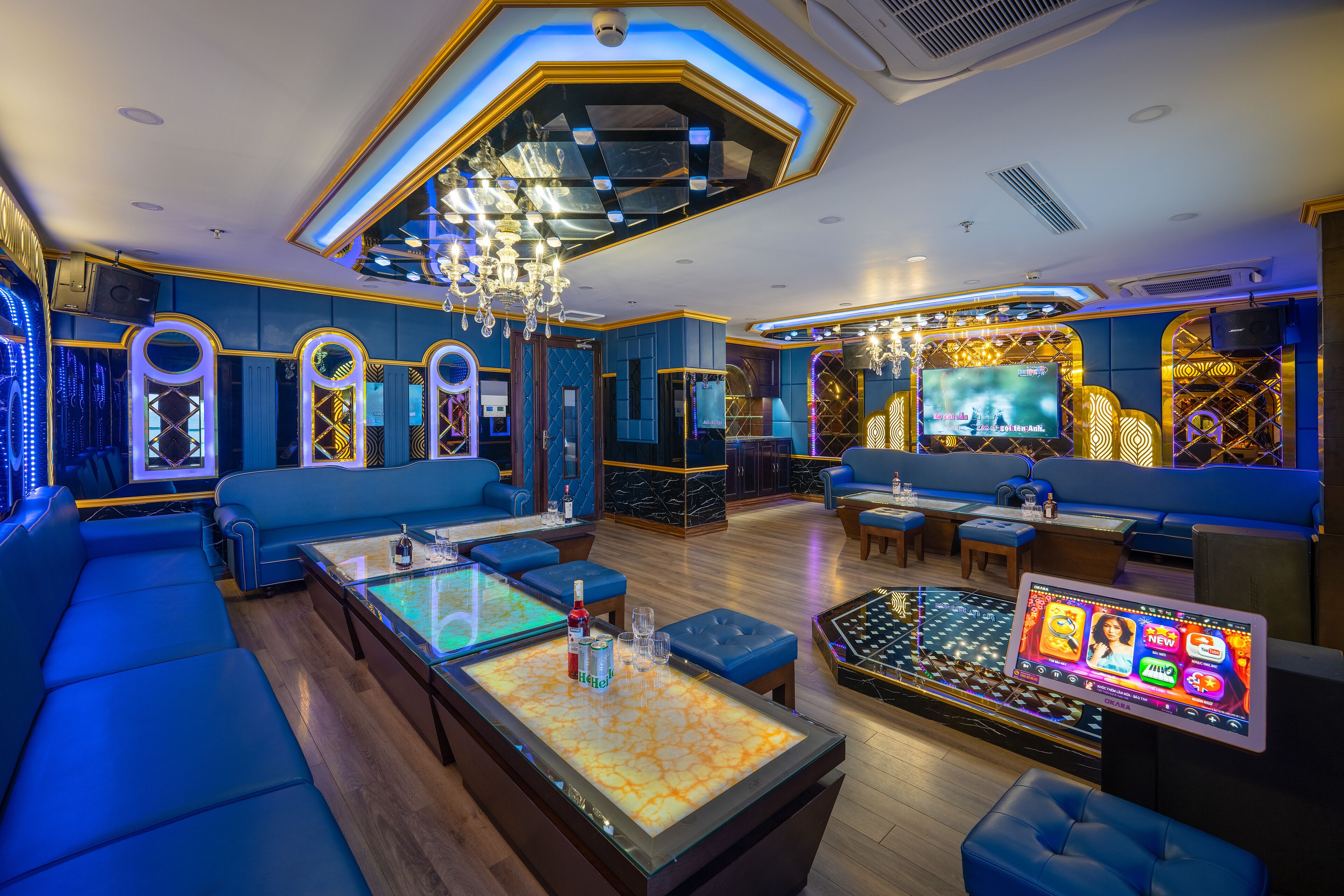 A modern lounge with blue seating, a central table with a screen, and a chandelier.