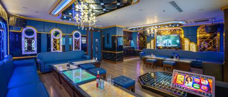 A modern lounge with blue seating, a central table with a screen, and a chandelier.