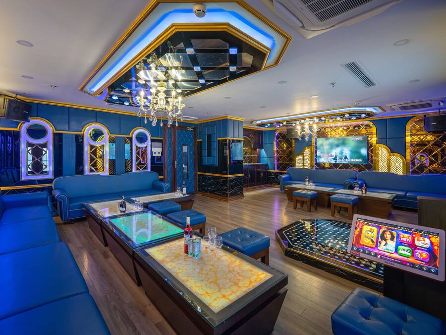 A modern lounge with blue seating, a central table with a screen, and a chandelier.