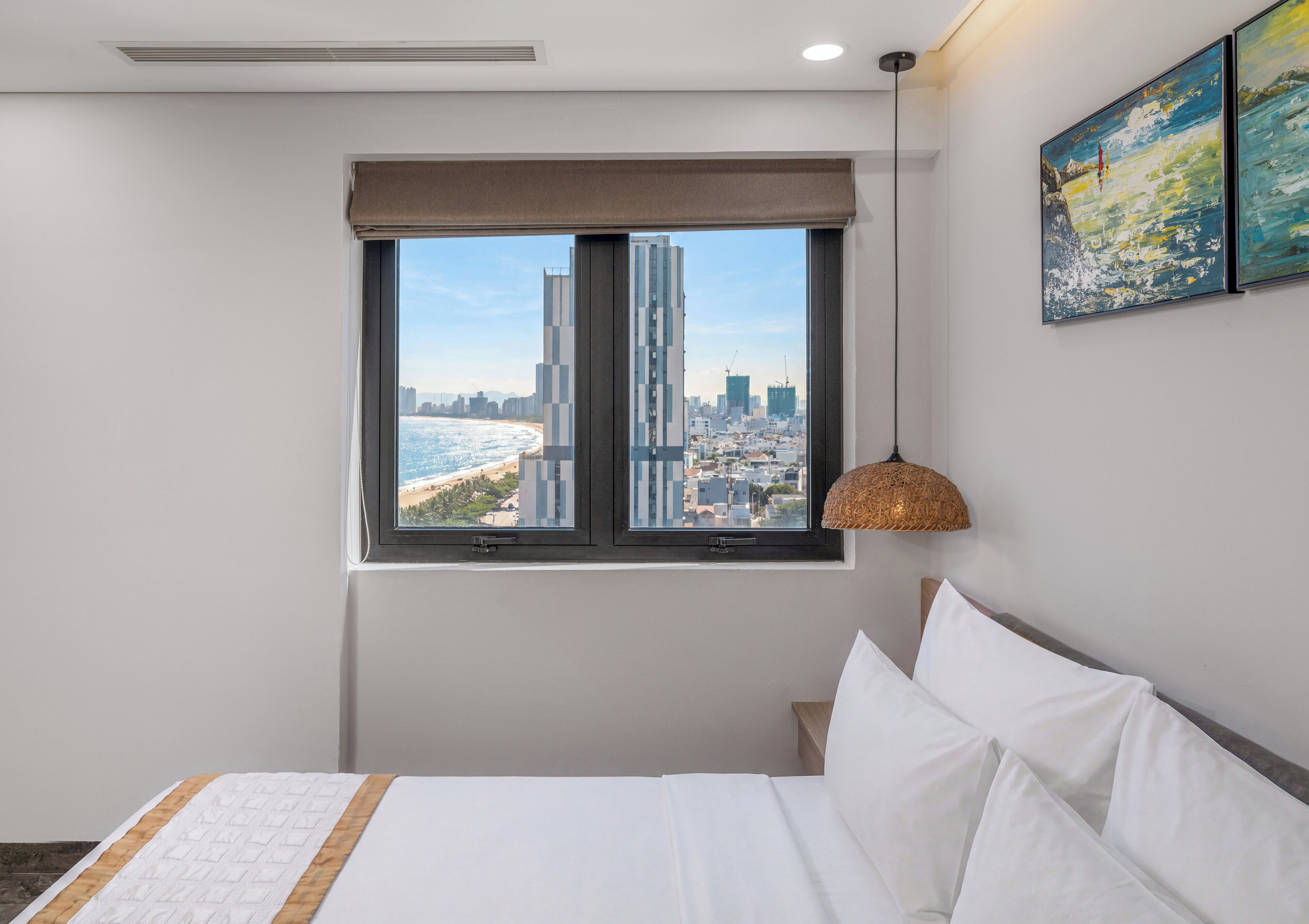 Habitación de hotel con cama, ventana con vistas a un paisaje urbano y una lámpara colgante.