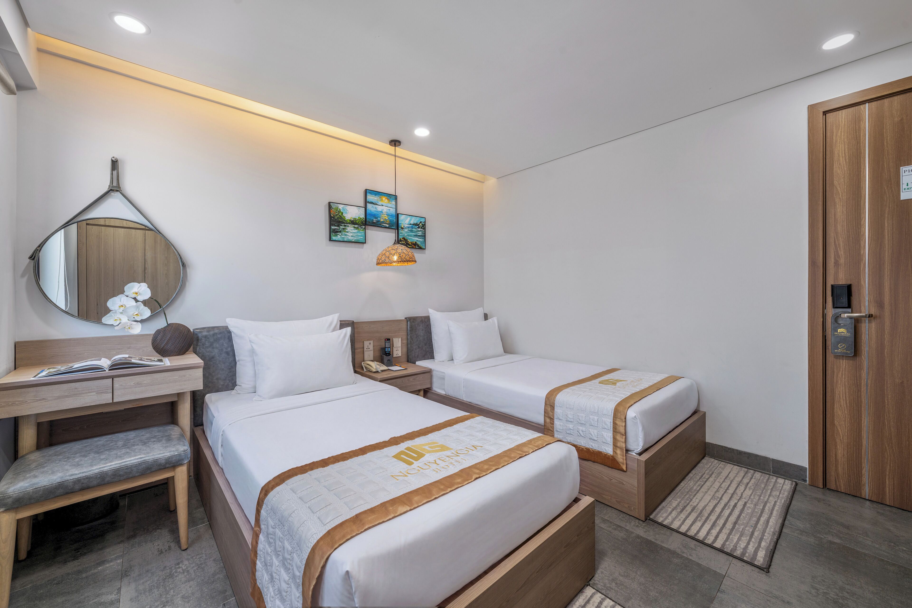 Habitación de hotel con dos camas, un escritorio, una silla, un espejo y obras de arte en la pared.