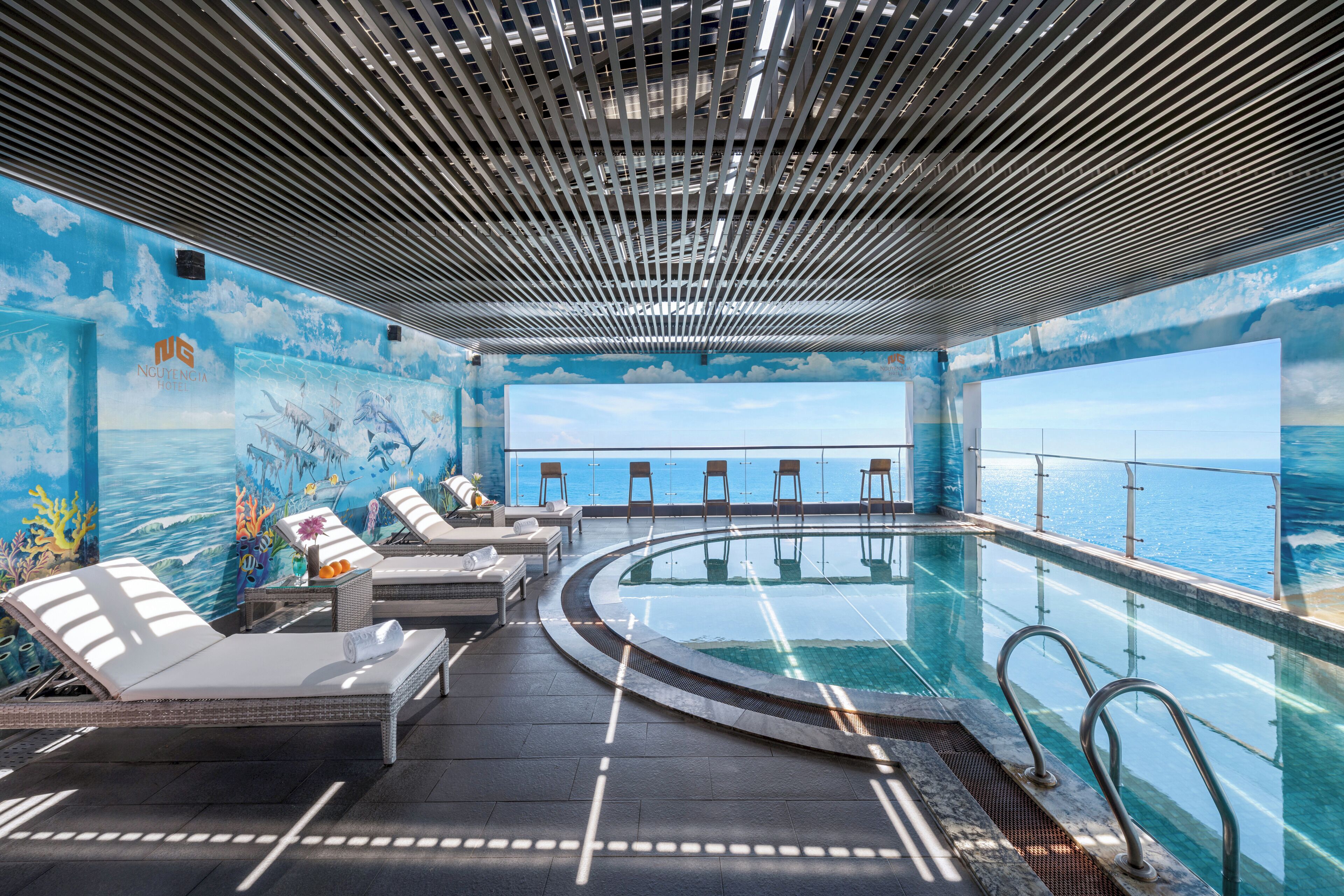 Zona de piscina con sillones de descanso, vista al mar y techo con diseño de cuadrícula.