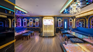 A modern lounge area with a central seating area, a bar with stools, and a large screen displaying content. - Nguyen Gia Hotel (Da Nang)