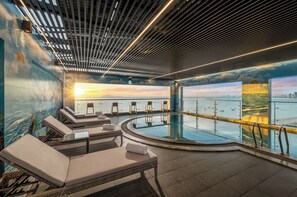 Zona de piscina interior iluminada por el sol con sillones de descanso y vistas al mar.