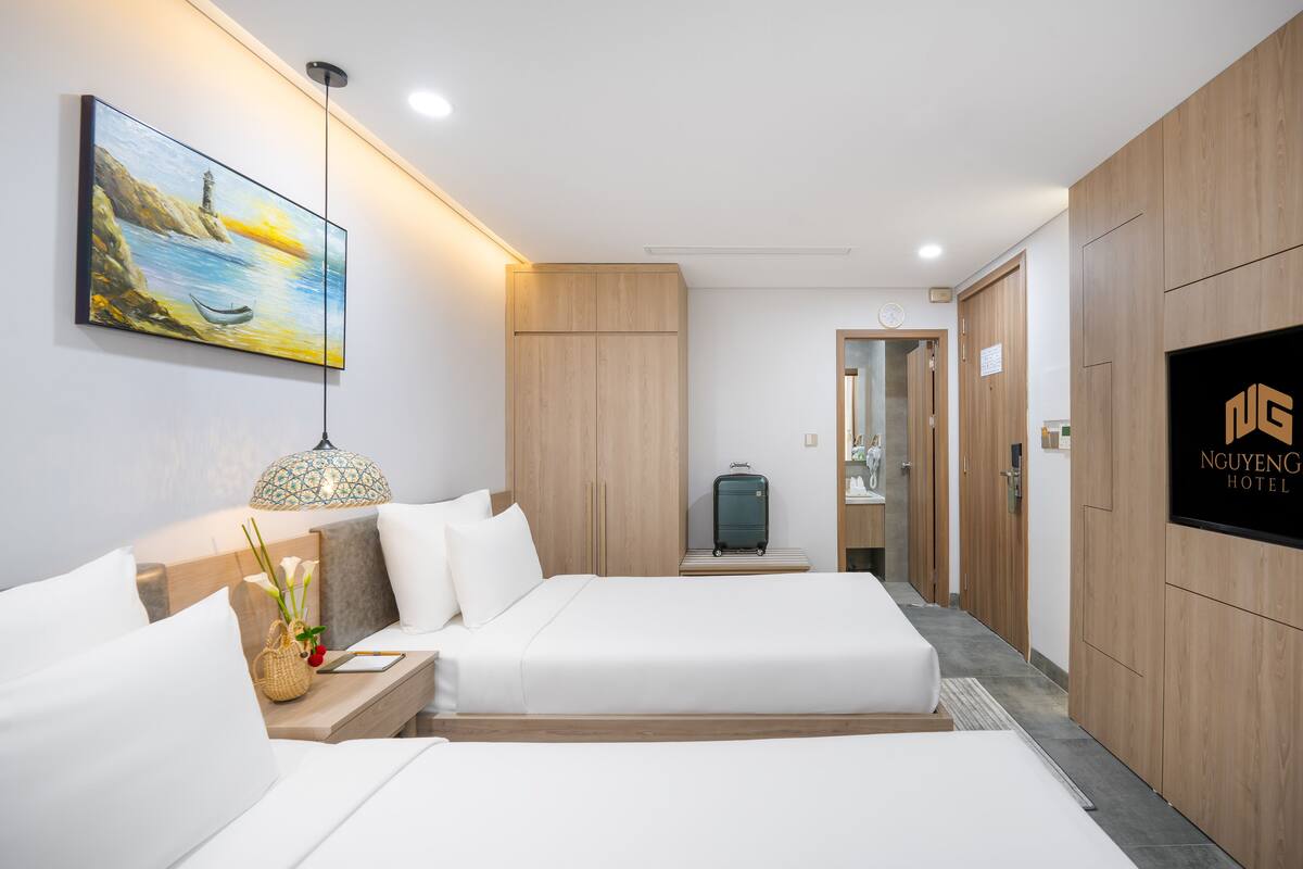 A hotel room with two beds, a painting on the wall, a lamp, and a TV on the wall.