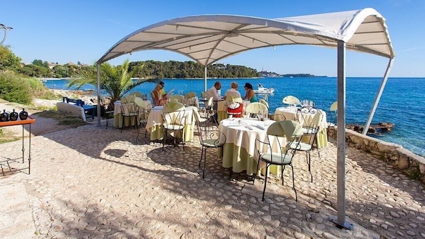 An outdoor dining area with tables and chairs, a covered seating area, and a view of the sea. - Apartment 1, located 200 meters from the sea in character house.  (Rovinj Borik)