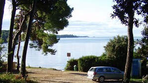 A paved path leading to a parking area with a car, trees, and a body of water in the background. - Apartment 1, located 200 meters from the sea in character house.  (Rovinj Borik)