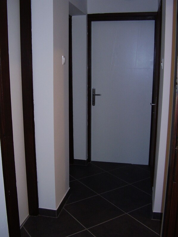 A hallway with a closed door, white walls, and dark tiled flooring.
