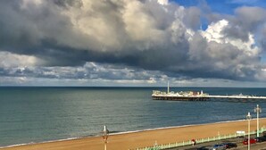 A beach with a pier extending into the sea, under a partly cloudy sky.
