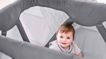 A baby enjoys playtime on a table or bed, surrounded by a soft cushion.