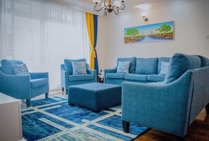 A modern living room with a blue sofa set, matching ottoman, and a patterned rug. - Luxel Suites by Homes by Della (Nairobi)