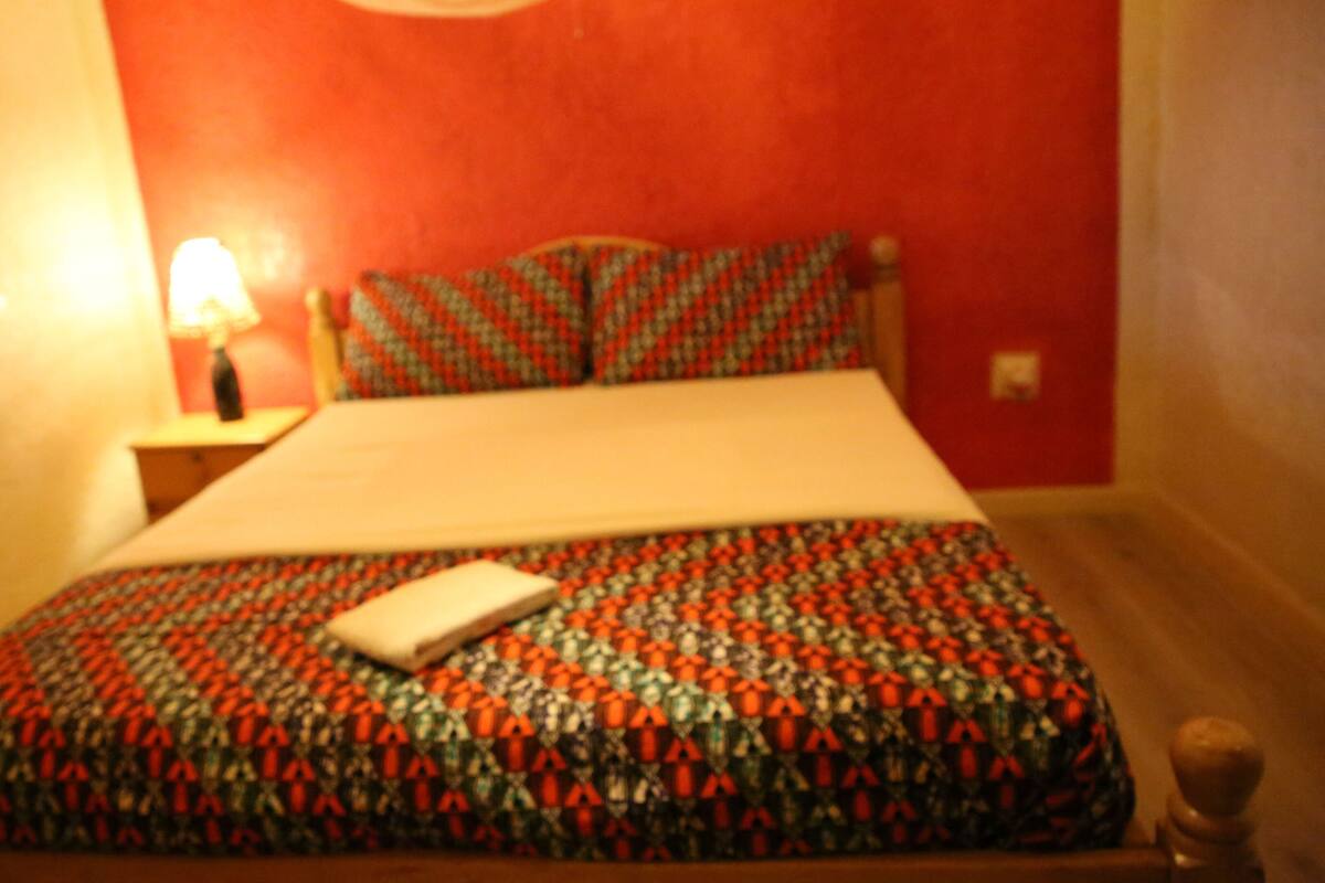 A bed with a patterned bedspread, a bedside table with a lamp, and a red wall.