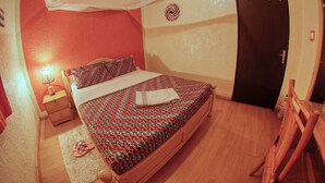 A bedroom with a bed, a nightstand, a wooden chair, a mosquito net, and a door. - Tea House BnB Apartment (Kigali)
