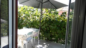 Un patio al aire libre con una mesa y sillas bajo un amplio paraguas, rodeado de abundante follaje verde.