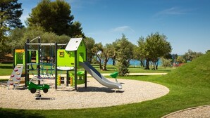 Un parque infantil con tobogán y estructuras para escalar, rodeado de césped y árboles.