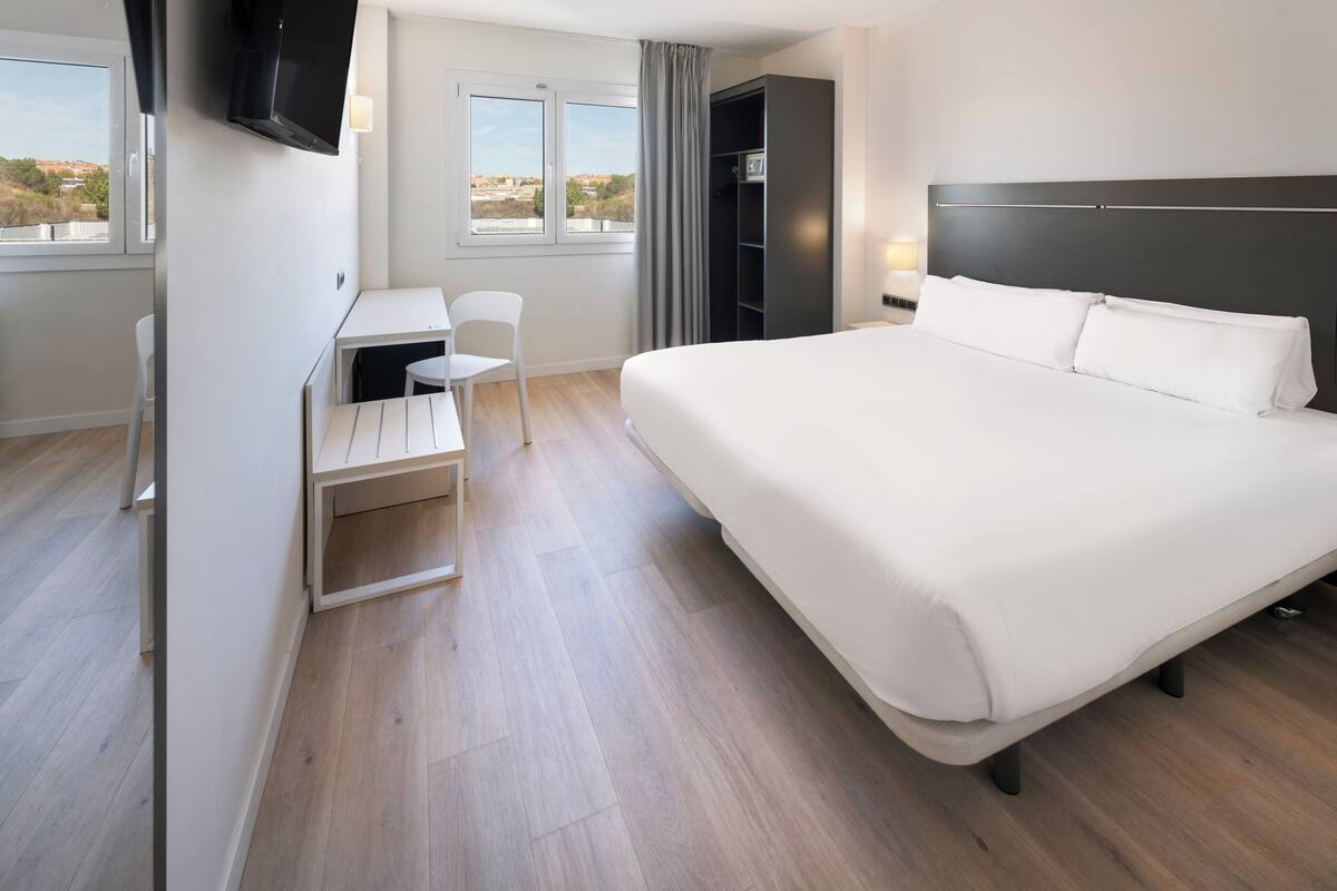 Habitación de hotel con una cama grande, un escritorio, una silla y un televisor montado en la pared.