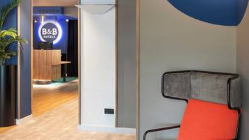 A modern hotel lobby with a reception desk, a blue accent wall, and orange seating.