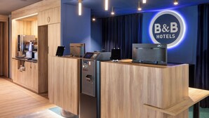 Zona de recepción de hotel con muebles de madera, un quiosco digital y el letrero de B&B Hotels.