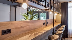 Un moderno bar con mostrador de madera, taburetes, iluminación colgante y un amplio ventanal con planta.