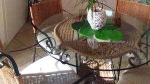 A dining area with a round glass table, wicker chairs, and a potted plant. - STUDIO APARTMENT WITH GARDEN VIEW (Scicli)