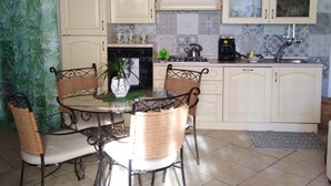 A kitchen with a round dining table, chairs, and a hanging light fixture. - STUDIO APARTMENT WITH GARDEN VIEW (Scicli)