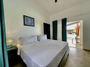 Habitación de hotel con una cama grande, una mesita de noche, un cuadro enmarcado en la pared y vistas al exterior a través de una puerta.