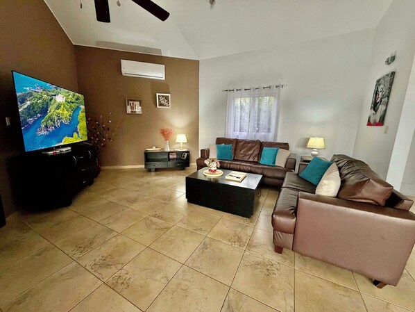 Una sala de estar con un televisor de pantalla plana, un sofá de cuero marrón, una mesa de centro y un mueble para televisión.