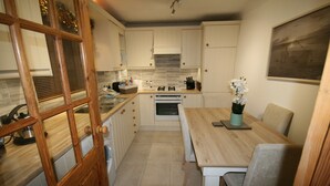 Una cocina con armarios blancos, una puerta de madera, una mesa de comedor con sillas y un jarrón con flores.