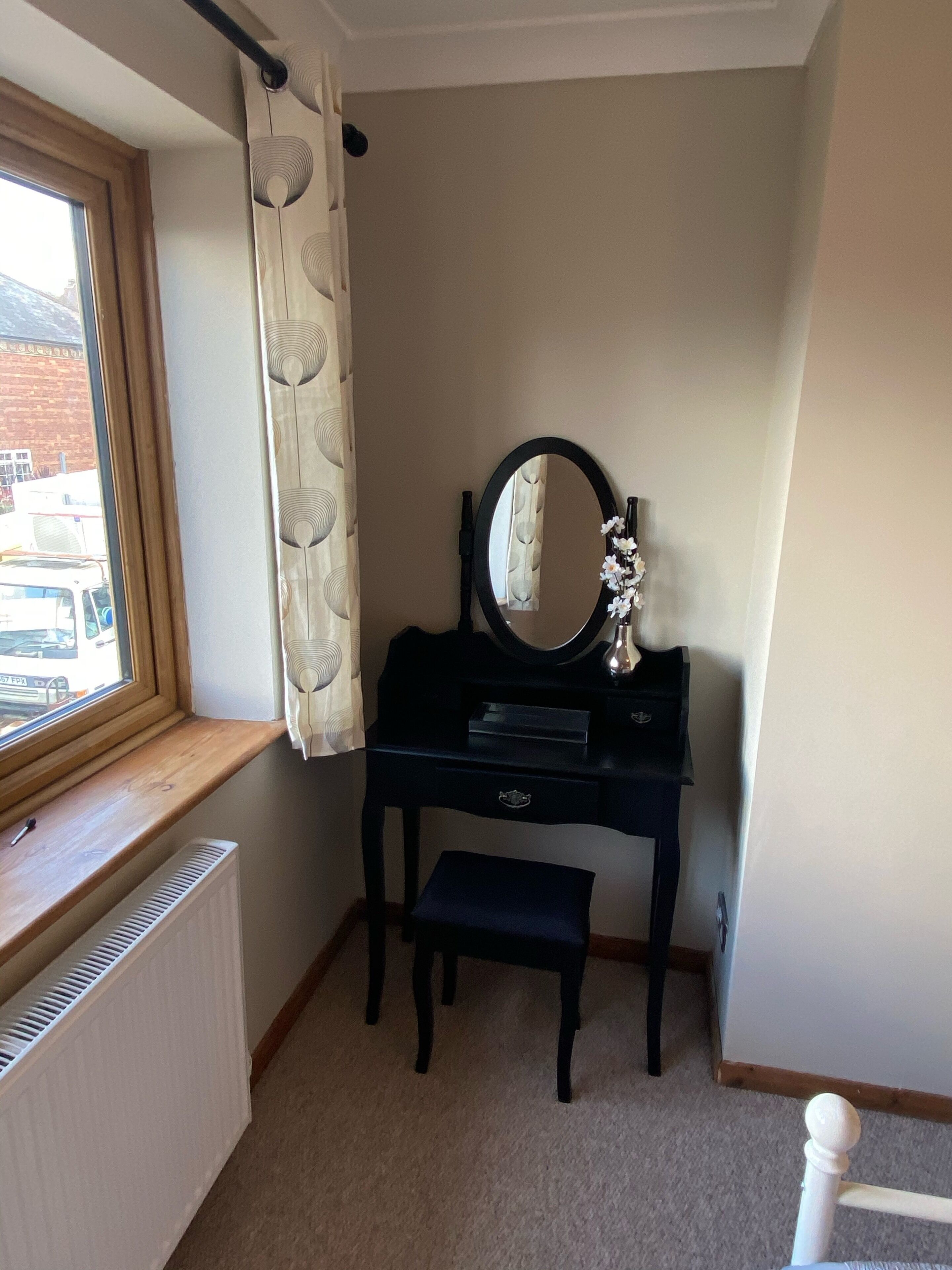 Une pièce de taille modeste, avec un rebord de fenêtre en bois, un bureau noir doté d’un miroir et un radiateur.