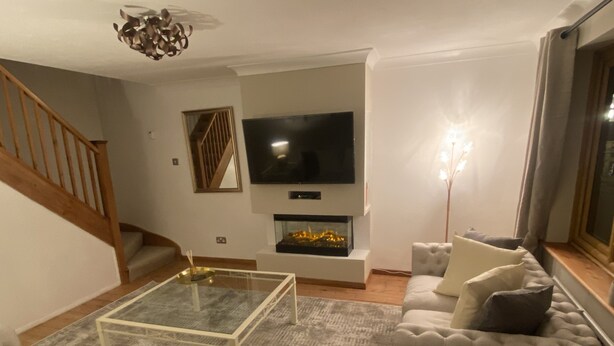 Una sala de estar con un sofá, una mesa de centro de vidrio, una chimenea, un televisor y una escalera.