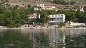A waterfront property with a view of the sea, a stone pathway, and a row of buildings with red roofs. - Hotel Val  (Seget)