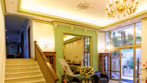 A grand staircase with a red rope barrier, a chandelier, and a large mirror in a well-lit lobby area. - Hotel Val  (Seget)