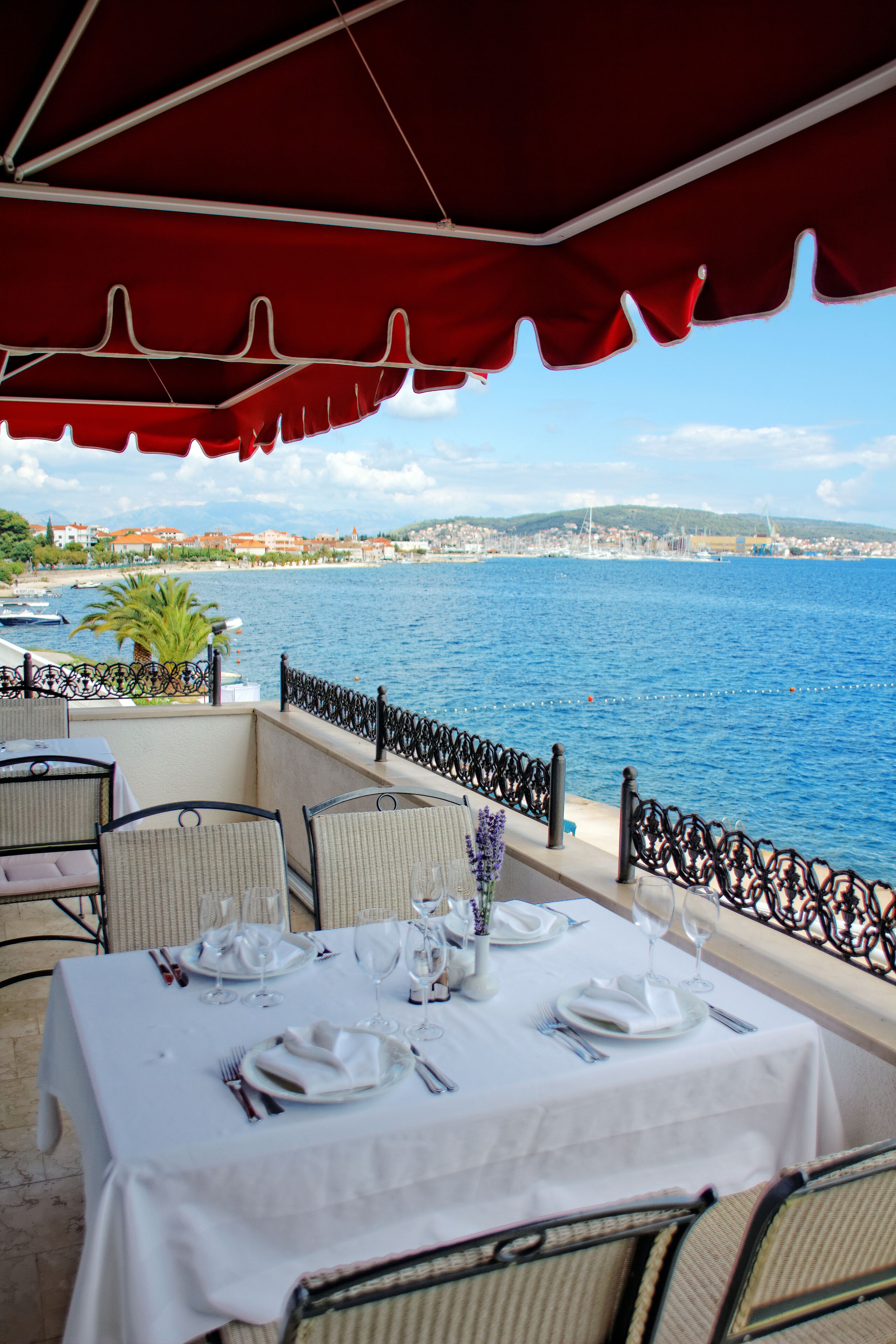 Area pranzo all'aperto con tavoli apparecchiati per un pasto, con vista su un corso d'acqua e un panorama urbano in lontananza.