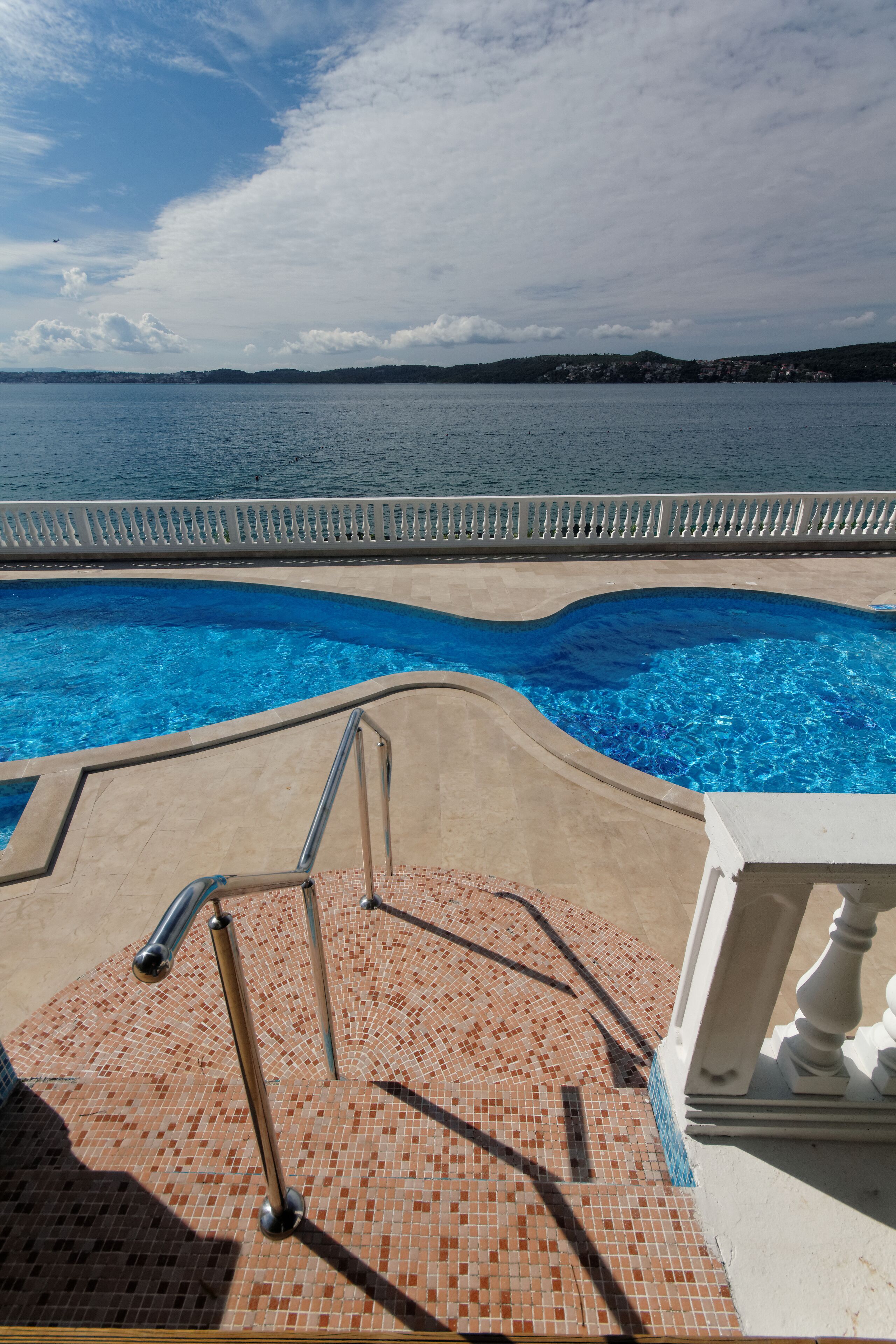 Une piscine à l’eau d’un bleu cristallin, une terrasse carrelée et une vue sur la mer et les collines lointaines.