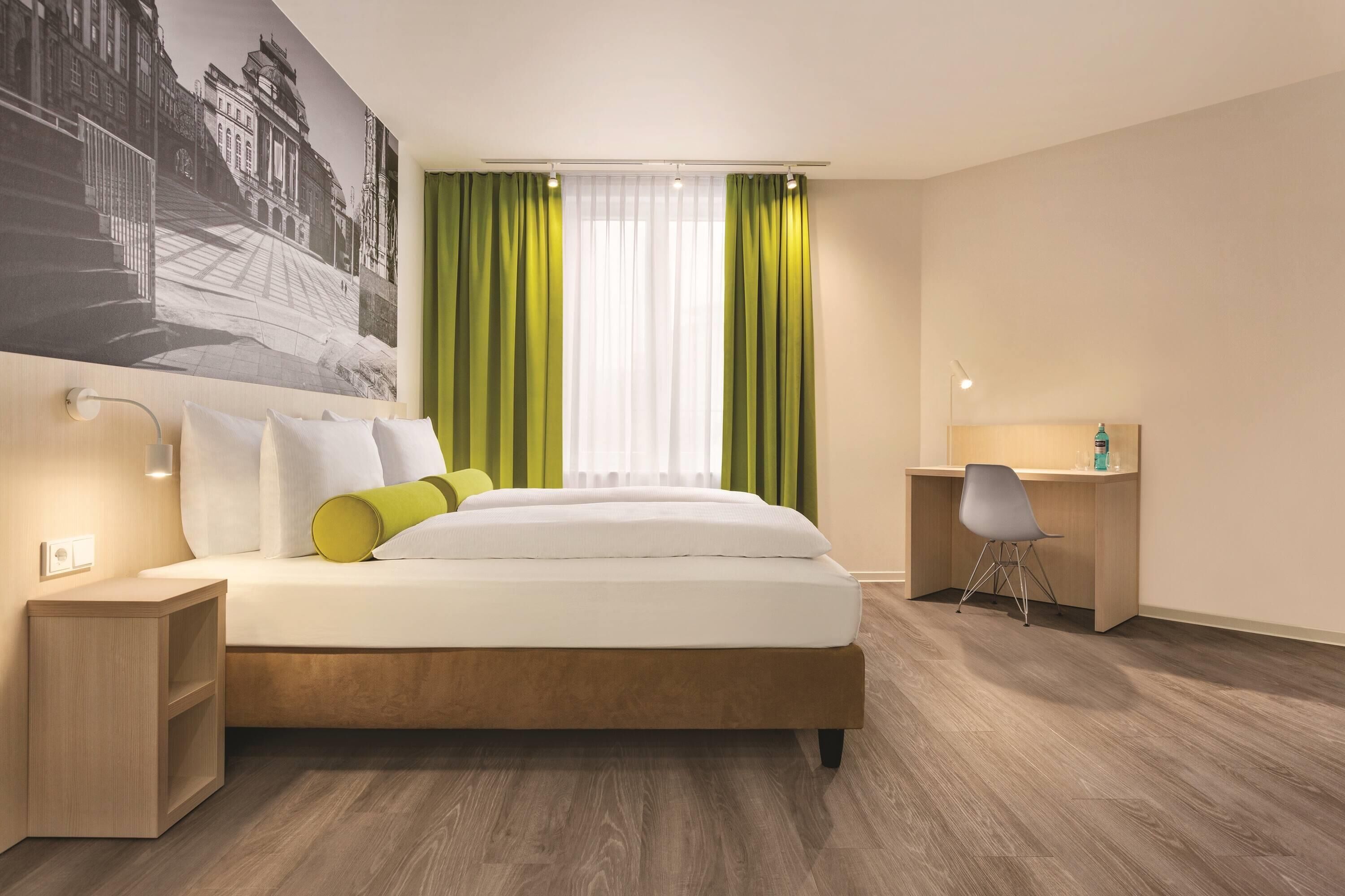 Quarto de hotel com cama, escrivaninha, cadeira e um grande mural na parede.