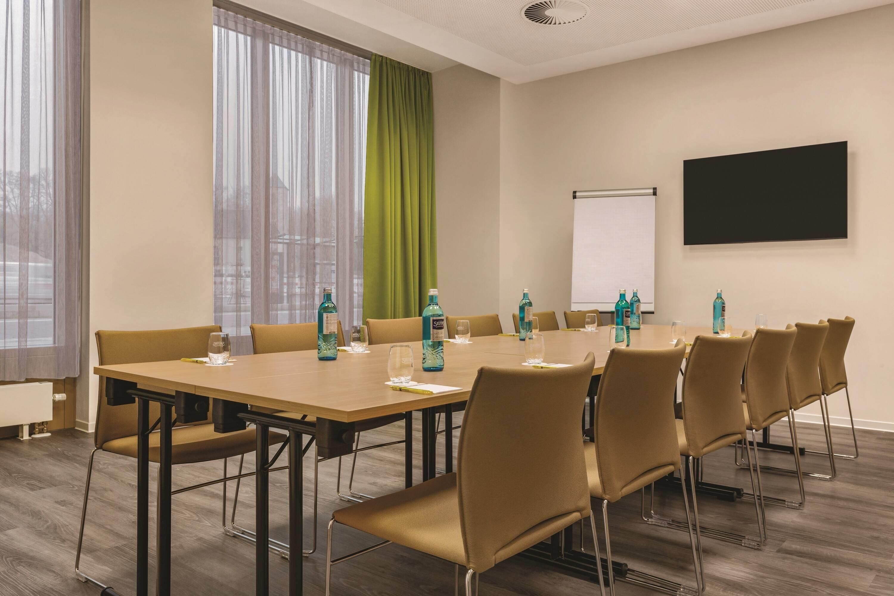 Ein Konferenzraum mit einem langen Tisch, Stühlen und einer Projektionsleinwand.