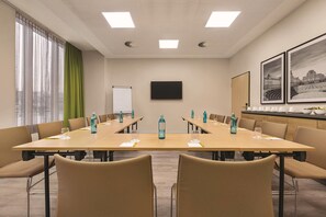 Een vergaderruimte met een lange tafel, stoelen, een whiteboard en ingekaderde foto's aan de muur.