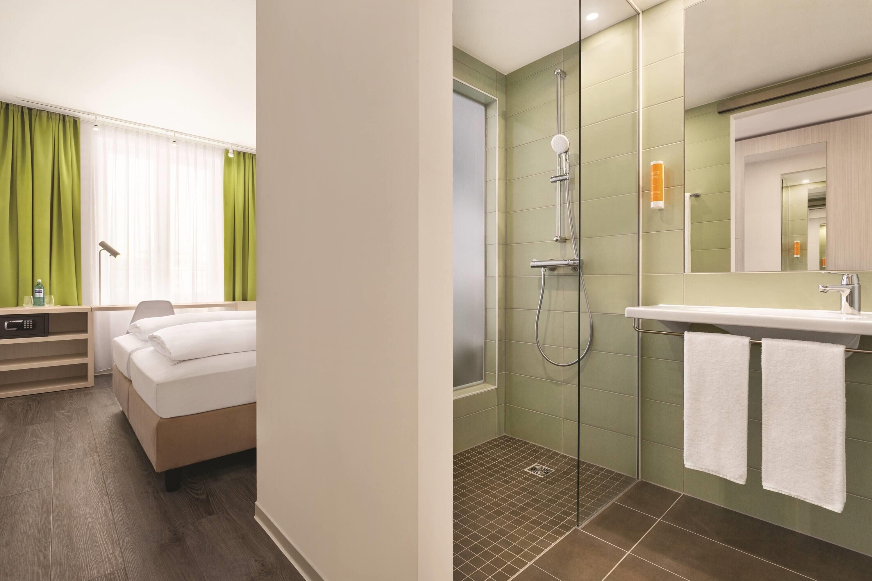 Ein Hotelzimmer mit Bett, Nachttisch, Lampe und einem Fenster mit Vorhängen.