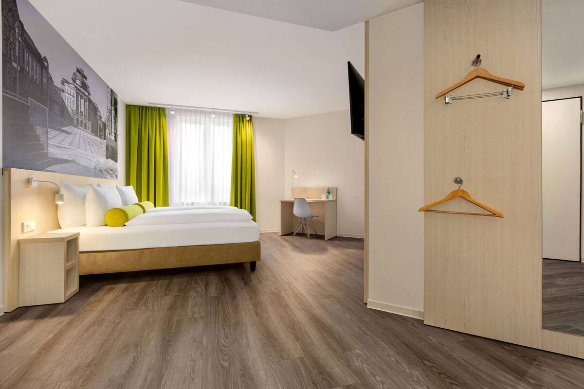 Une chambre d’hôtel moderne avec un grand lit, un bureau et une armoire avec un miroir.