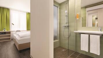 A hotel room with a bed, a bedside table, a lamp, and a window with curtains.