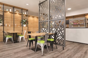 A modern dining area with a wooden table and chairs, a decorative partition, and a kitchen counter with jars. - Super 8 by Wyndham Chemnitz (Chemnitz)