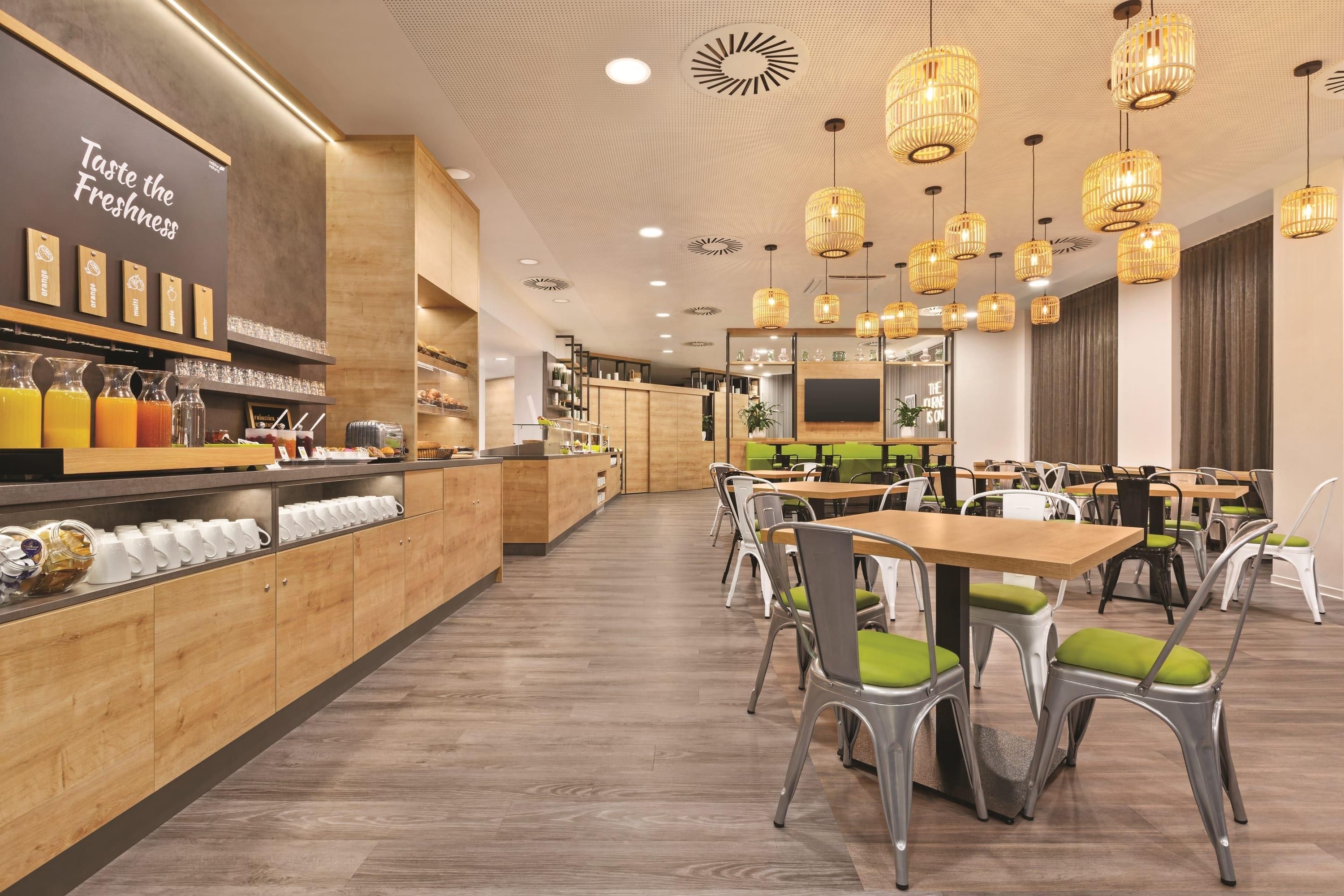 Interior de una cafetería moderna con mostradores de madera, diversas bebidas y una zona de estar con mesas y sillas.