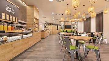 Interior de una cafetería moderna con mostradores de madera, diversas bebidas y una zona de estar con mesas y sillas.