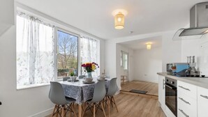 Una cocina moderna con armarios blancos, horno empotrado y comedor con mesa y sillas.
