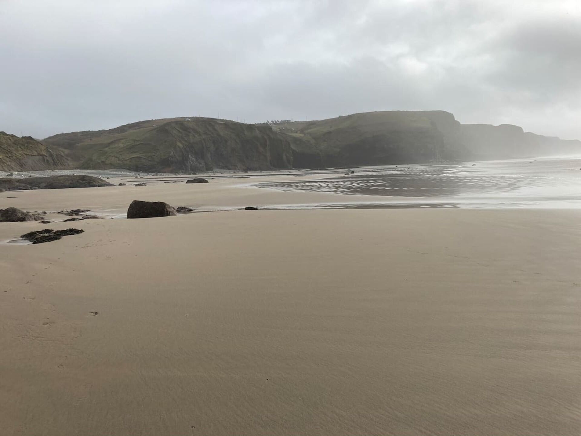 A beach with a sandy shore, scattered rocks, and a hilly landscape in the background.