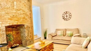 Una sala de estar acogedora con una chimenea de ladrillo, una mesa de centro de madera, un sofá color crema y un reloj de pared.