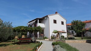 Un edificio blanco con tejado de tejas rojas, un sendero empedrado y un banco en un jardín ajardinado.