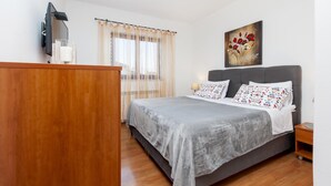 Un dormitorio con una cama, un aparador de madera, un televisor montado en la pared y un cuadro sobre la cama.