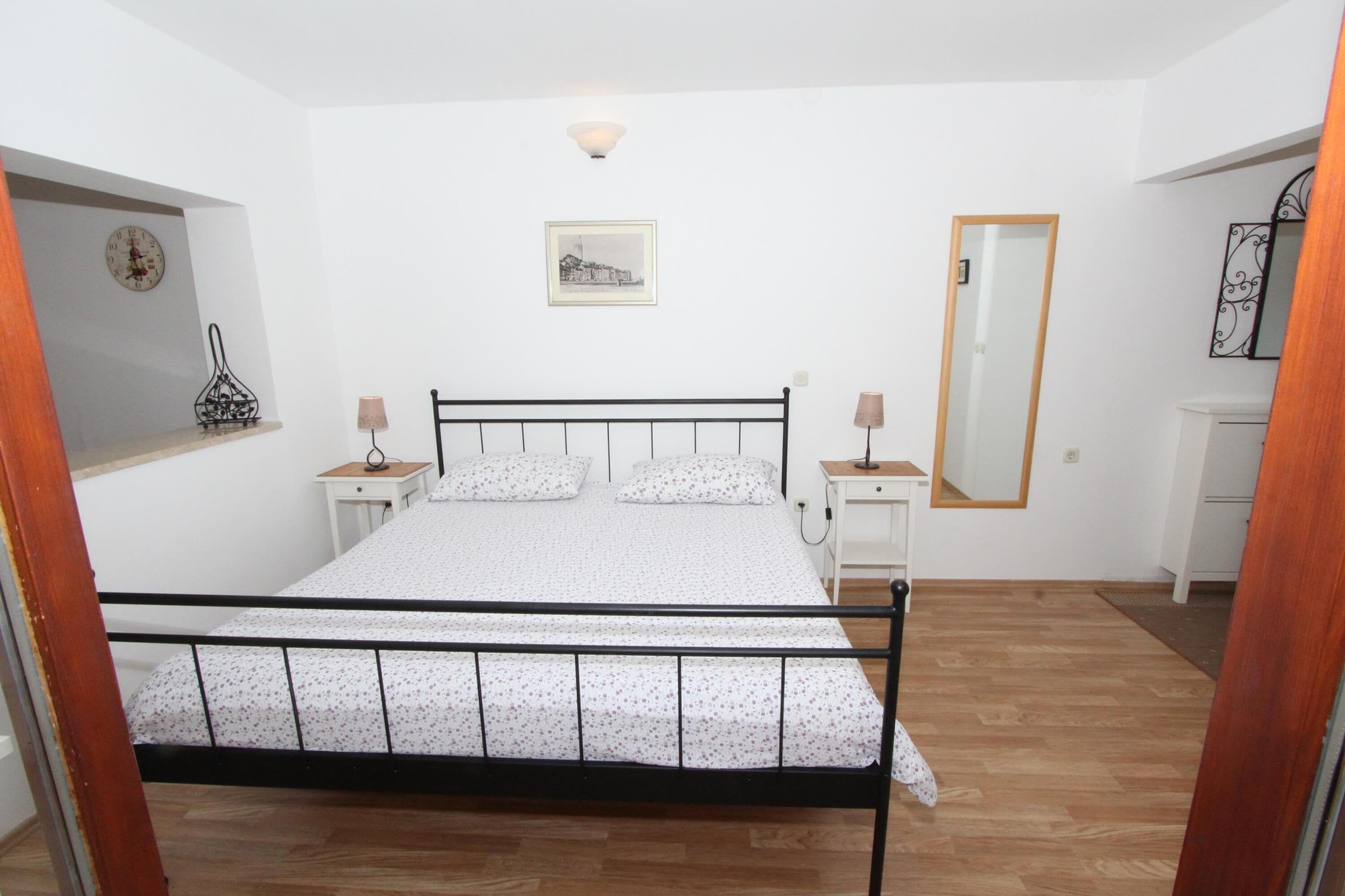 Une chambre à coucher avec un lit, des tables de chevet, un miroir, une horloge et un tableau encadré au mur.